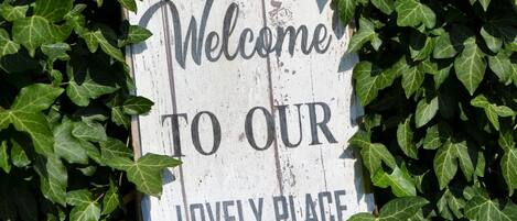 A wooden sign with the text "Welcome to our lovely place" surrounded by green ivy.