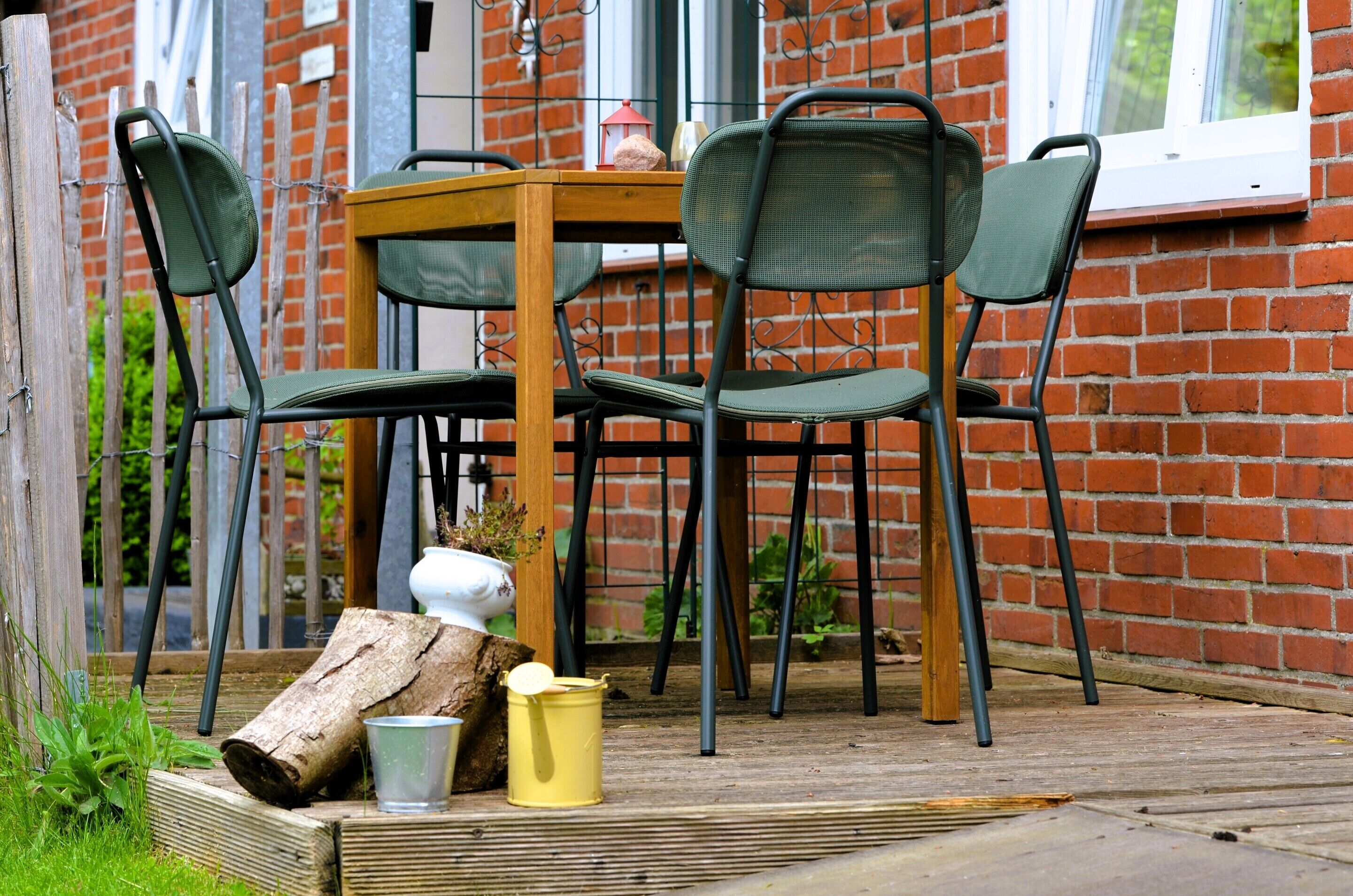 A wooden table with four chairs, a white vase, and a yellow bucket on a wooden deck.