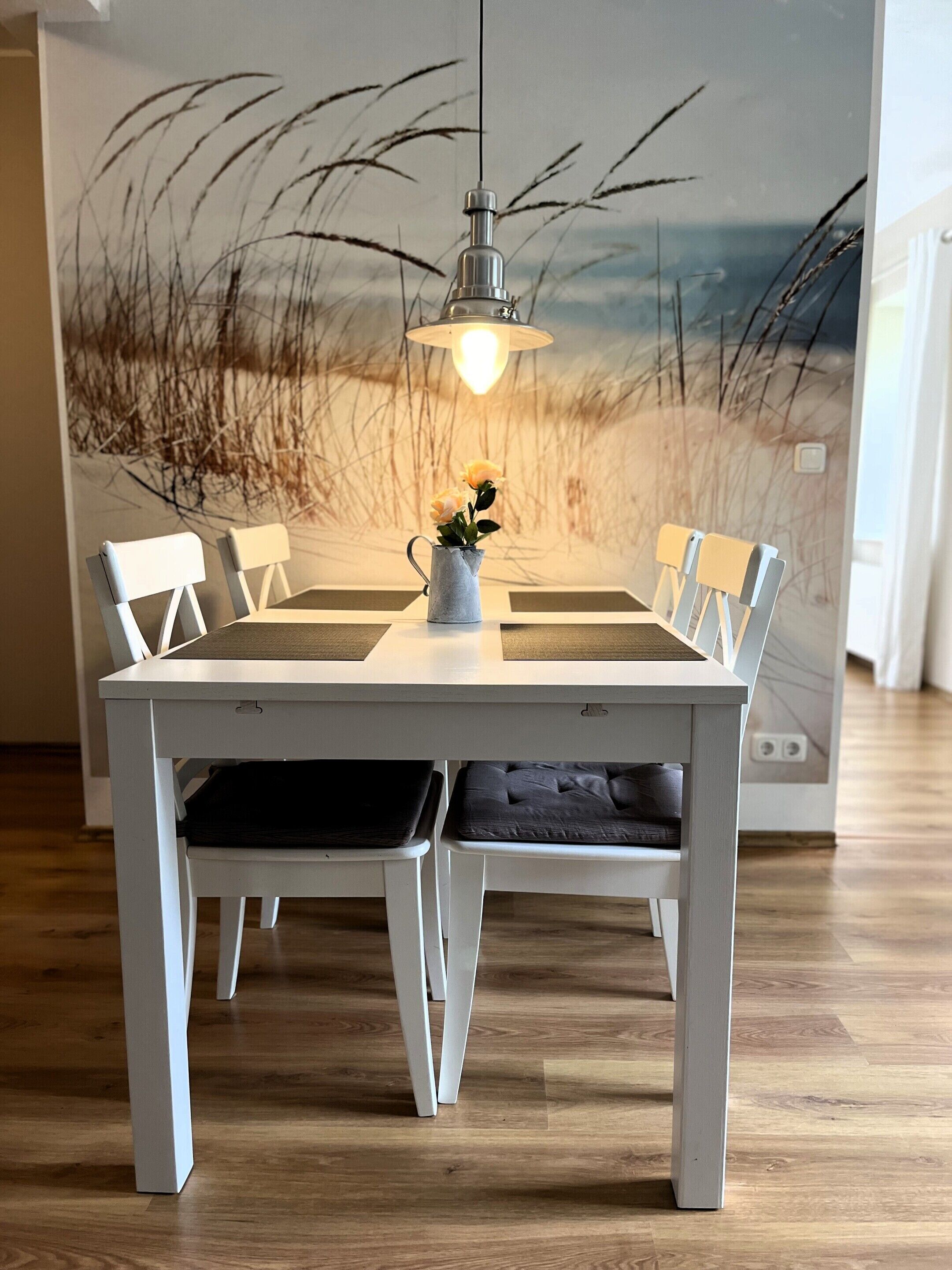 Een eettafel met witte stoelen en een vaas met bloemen.