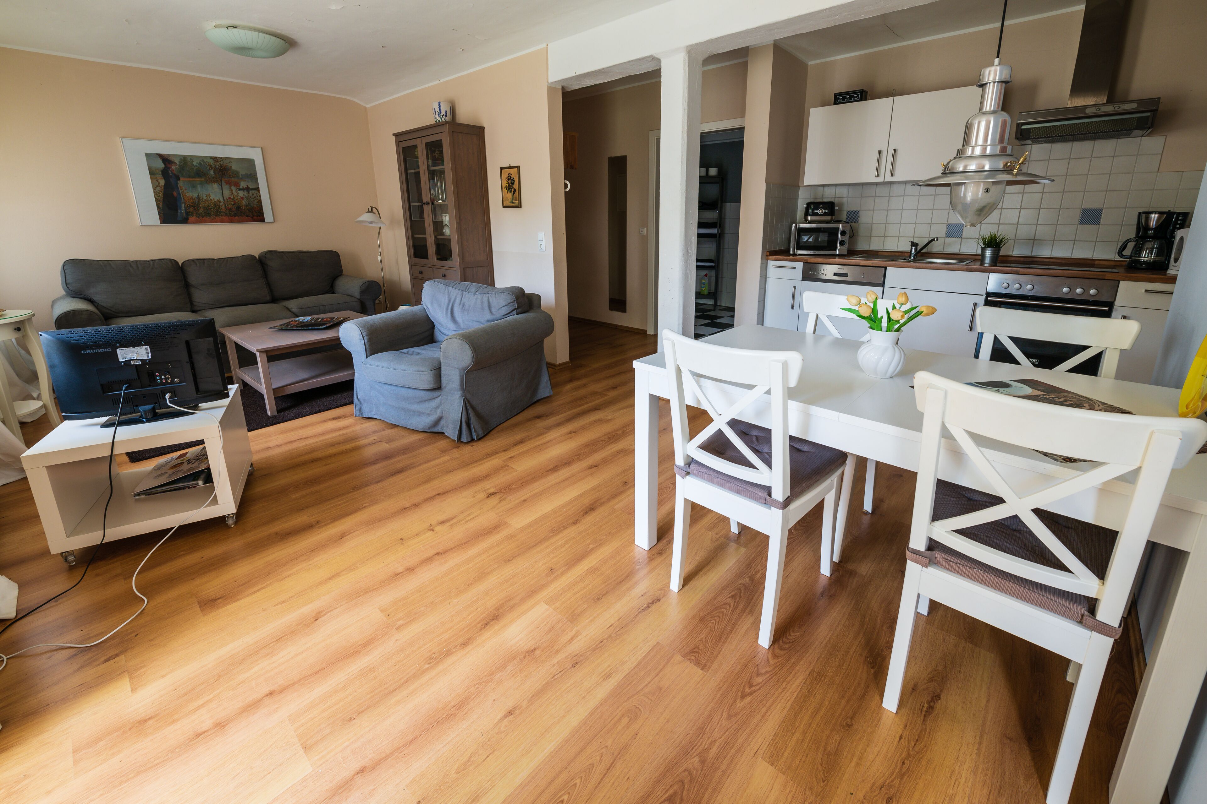 Una sala de estar con un sofá, una mesa de centro y un mueble para televisión. Hay una mesa de comedor con sillas y una zona de cocina con armarios y electrodomésticos.