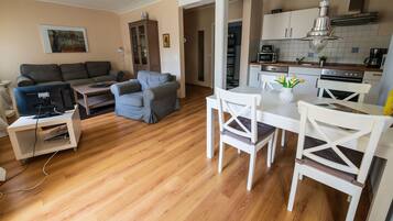 Una sala de estar con un sofá, una mesa de centro y un mueble para televisión. Hay una mesa de comedor con sillas y una zona de cocina con armarios y electrodomésticos.