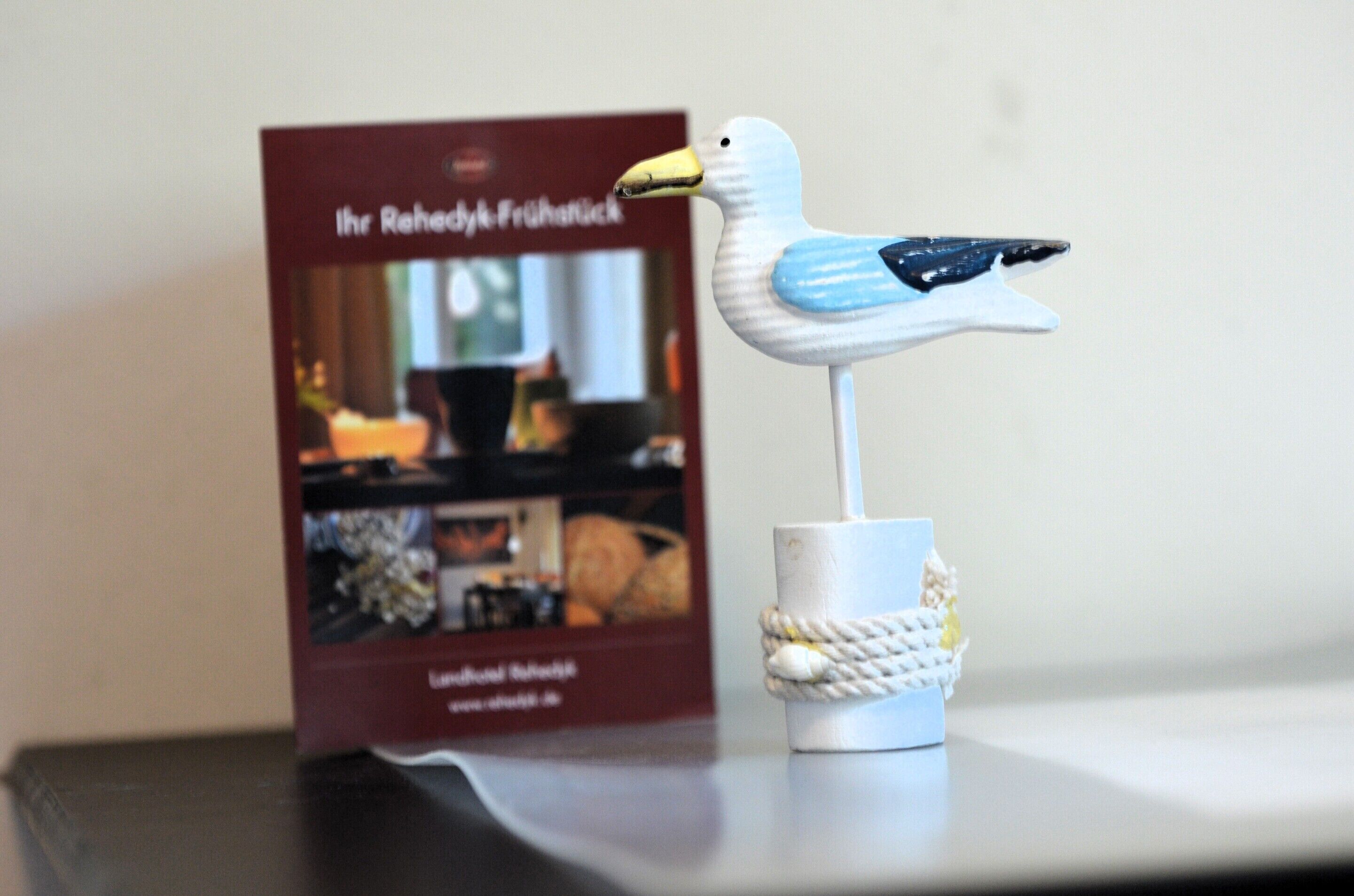Una figurita decorativa de gaviota sobre un pedestal blanco, junto a un libro titulado "Ihr Rehebyk Fruhnick".