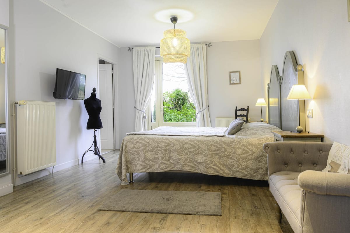 A bedroom with a bed, a dresser, a chair, a television, and a window with curtains.