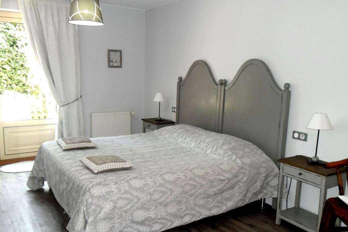 A bedroom with a bed, bedside tables, a lamp, a radiator, and a window with curtains.