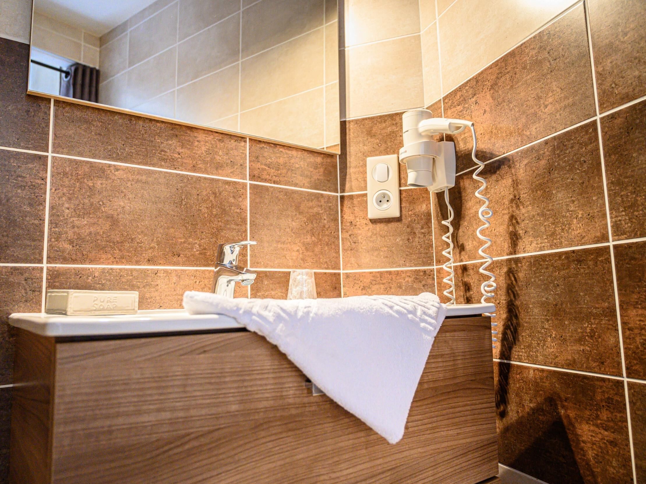 A bathroom with a wooden vanity, a white sink, a towel, and a wall-mounted light fixture.