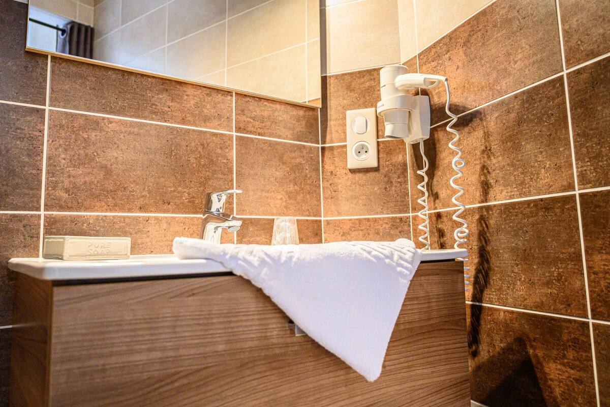 A bathroom with a wooden vanity, a white sink, a towel, and a wall-mounted light fixture.