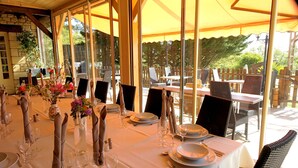 Un comedor con mesas dispuestas para una comida, con manteles blancos, servilletas dobladas y cristalería.
