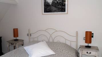 A bedroom with a bed, two bedside tables with lamps, a wall-mounted picture, and a power outlet.