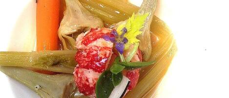 Un plat composé d’une carotte, d’un morceau de viande et d’une fleur, le tout présenté sur une assiette blanche.