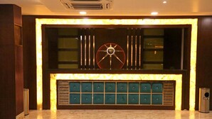 A lobby with a marble floor, a large wall-mounted clock, and a seating area with green cushioned benches. - Hotel Varanasi Inn (Varanasi)