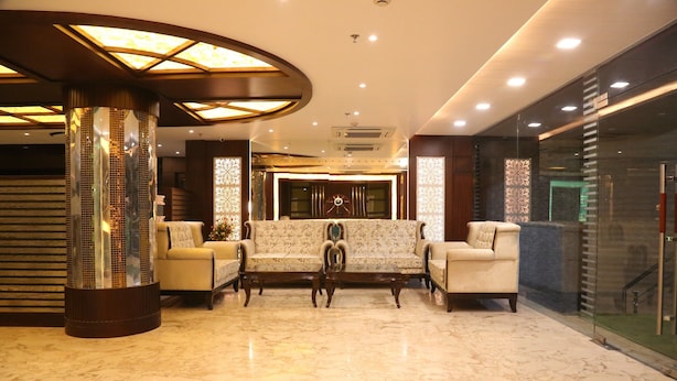 A lobby with a marble floor, a sofa set, a decorative pillar, and a glass partition. - Hotel Varanasi Inn (Varanasi)