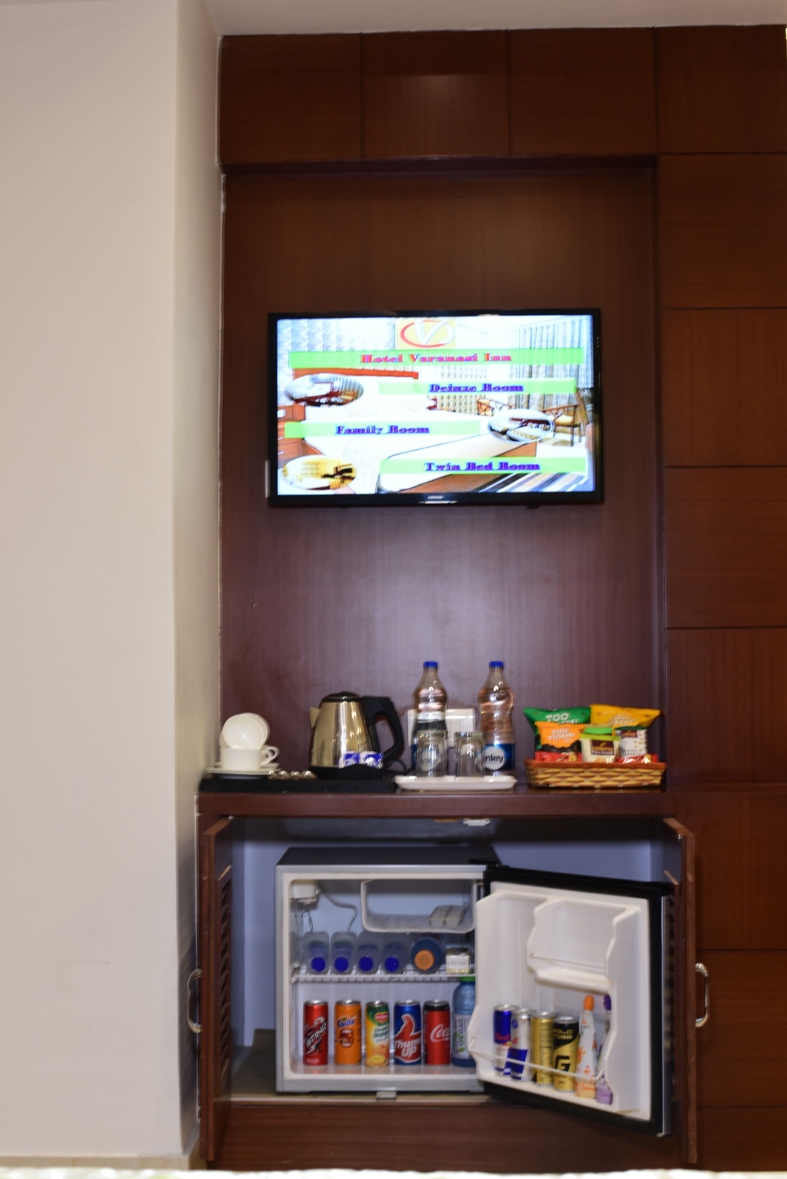Un televisore montato a parete sopra un mini-frigo pieno di bevande.