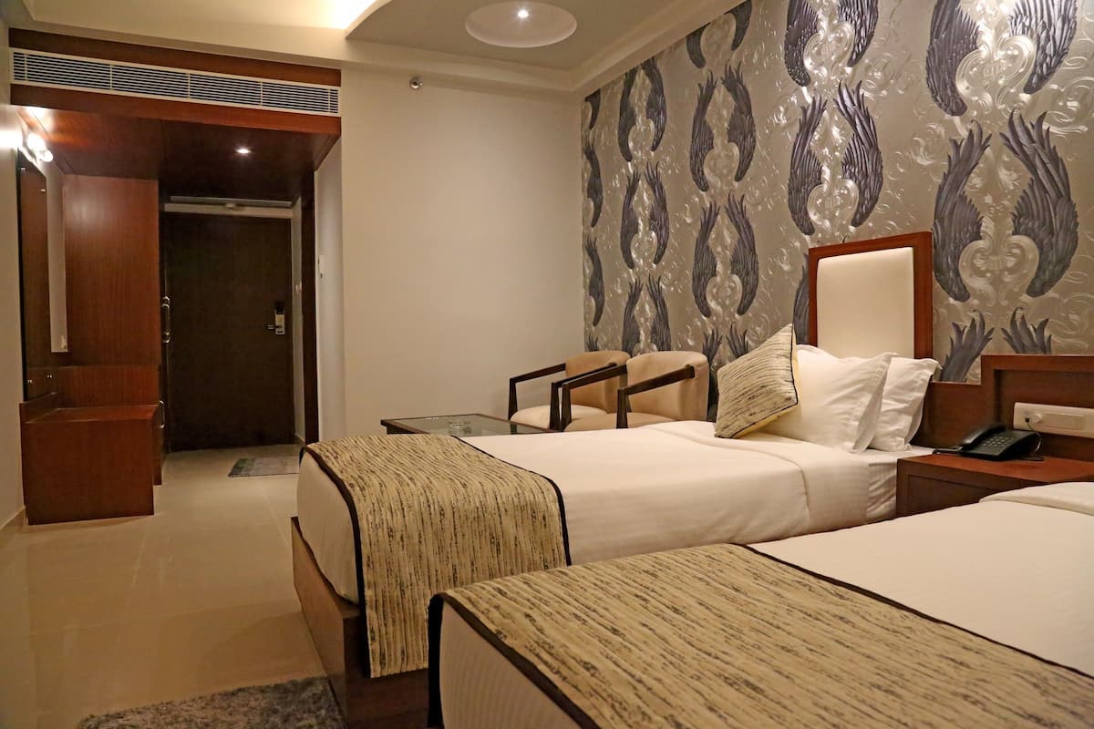 Habitación de hotel con dos camas, un armario de madera, una mesa de vidrio y un papel tapiz estampado.