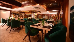 A restaurant with green upholstered chairs, white tables, and a marble floor. - Hotel Varanasi Inn (Varanasi)