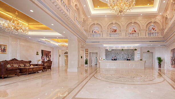 A spacious lobby with a grand chandelier, a reception desk, and a classic sofa.
