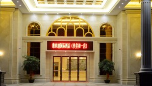 A hotel entrance with a large red sign, arched windows, and two potted plants.