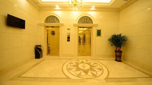 A lobby with a chandelier, two ornate doors, a television, a potted plant, and a decorative floor pattern.