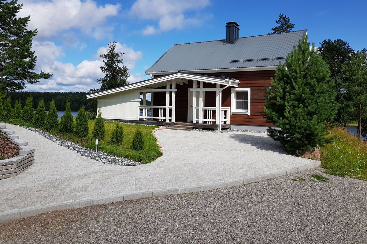 Een twee verdiepingen tellend huis met een veranda, schoorsteen en uitzicht op een meer.