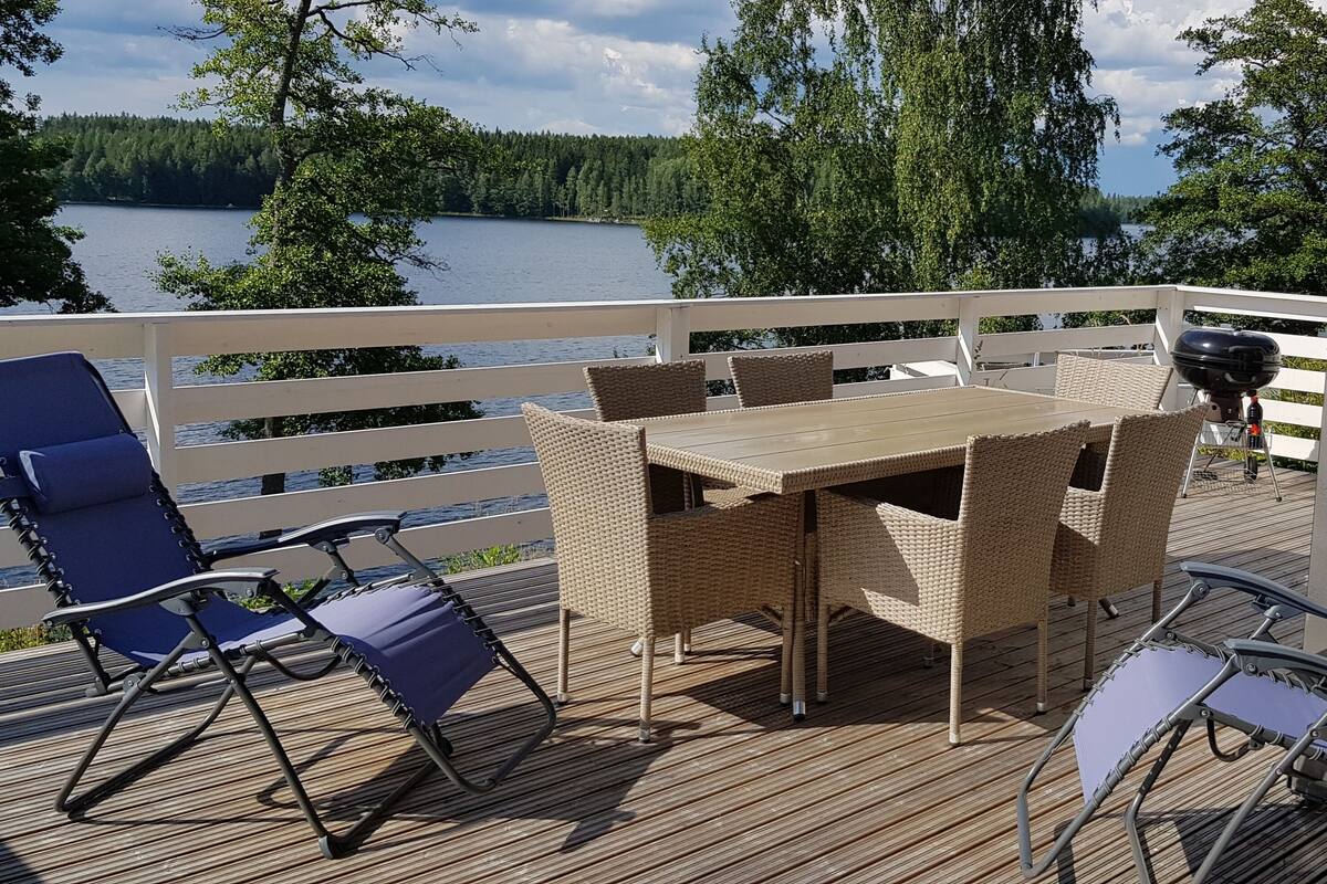 Een terras met een tafel en stoelen, met uitzicht op een meer en bos.