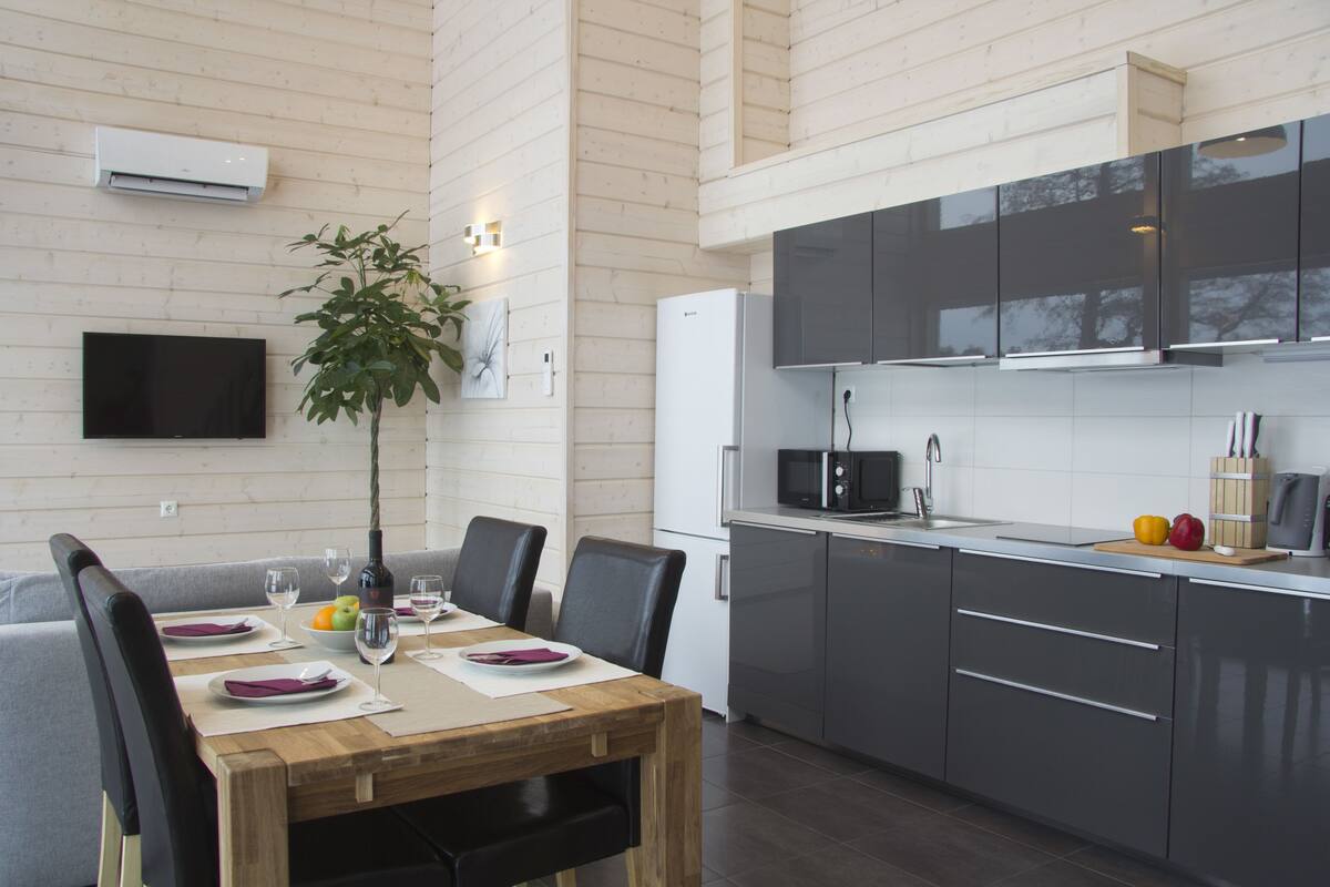 Een moderne keuken met grijze kastjes, een houten eettafel en een flatscreen televisie aan de muur.