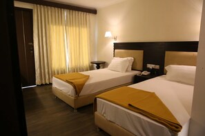 A hotel room with two beds, a bedside table with a lamp, and a window with curtains. - Hotel La Castle (Chennai)