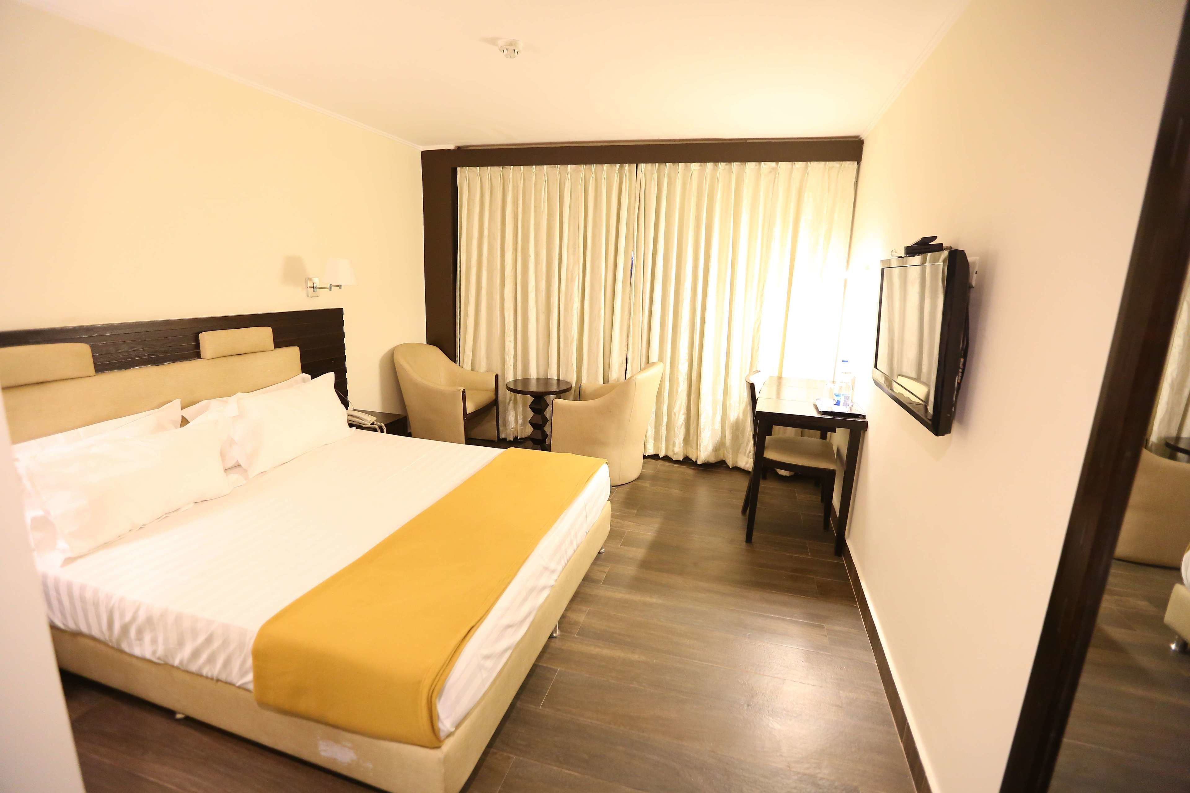 Une chambre d’hôtel avec un grand lit, un bureau avec une chaise, une télévision et une fenêtre avec des rideaux.