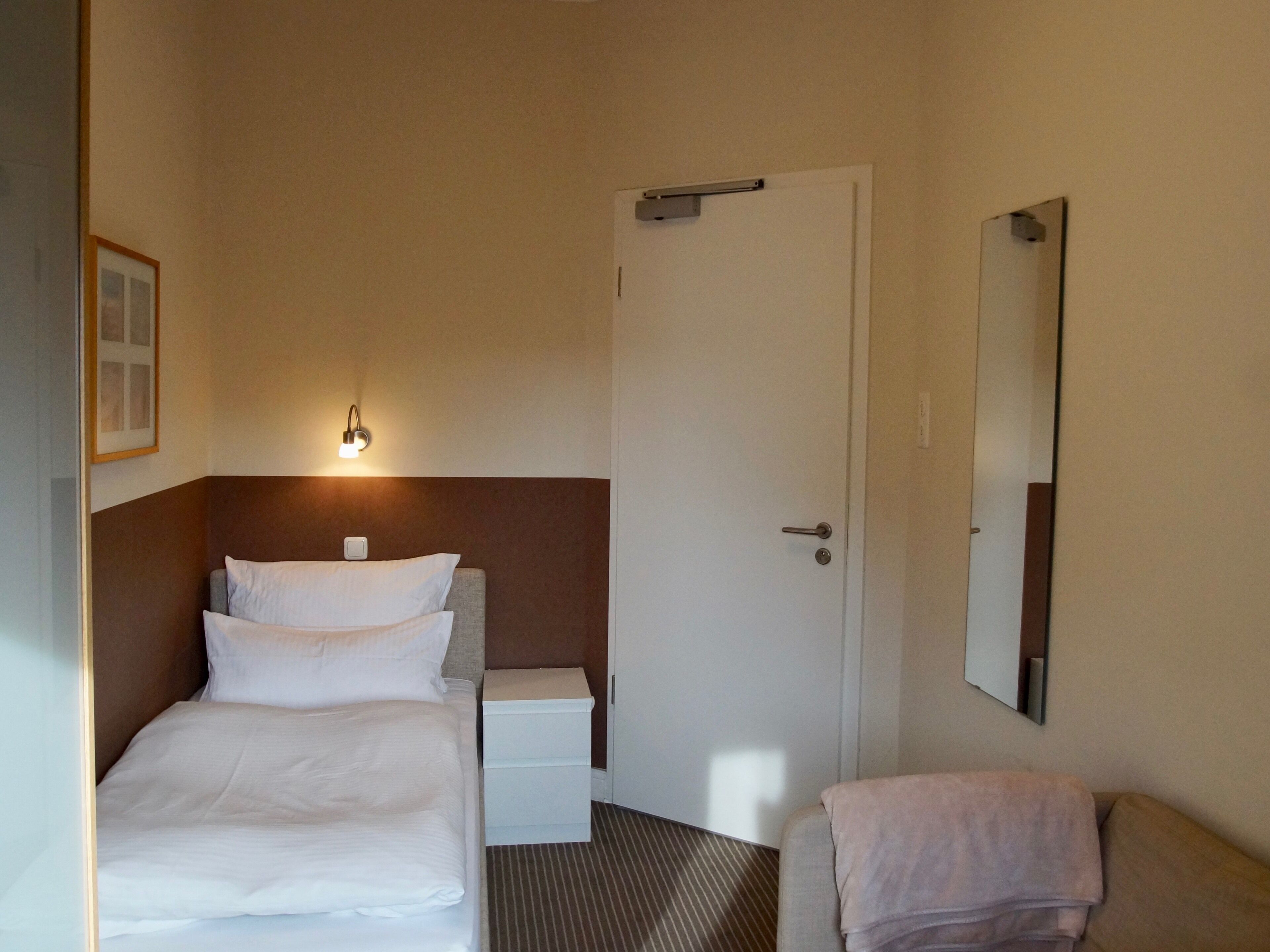Une chambre d’hôtel avec un lit, une table de chevet et un miroir au mur.