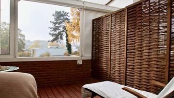 Una habitación con suelo de madera, una silla blanca, una mesa y vistas a través de una ventana.
