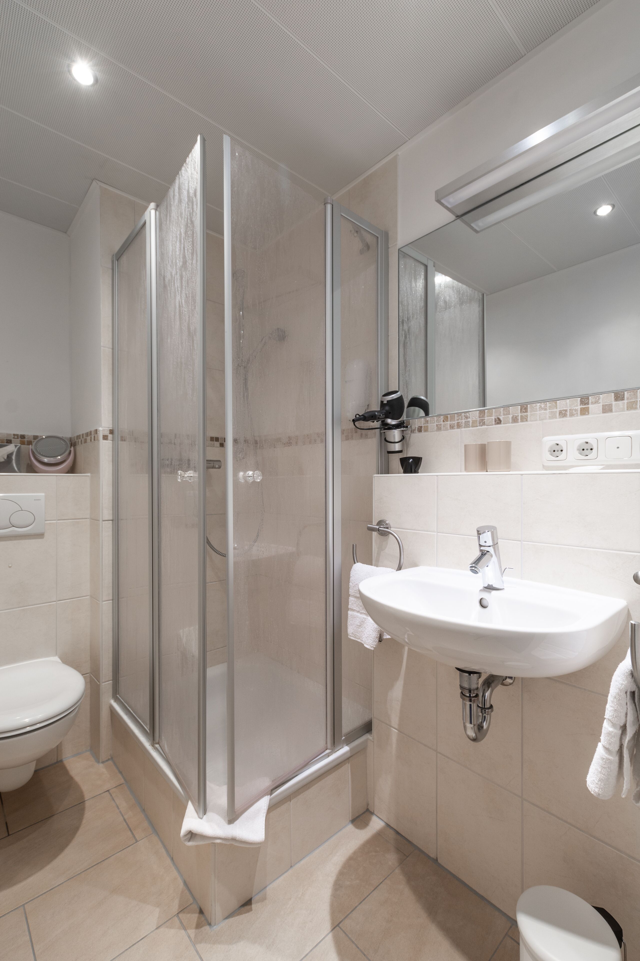 Un baño moderno con ducha acristalada, lavamanos blanco y retrete.