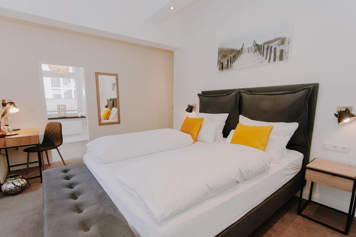 Ein Hotelzimmer mit einem großen Bett, einem Schreibtisch mit Stuhl, einem kleinen Tisch und einem Fenster mit Außenblick.