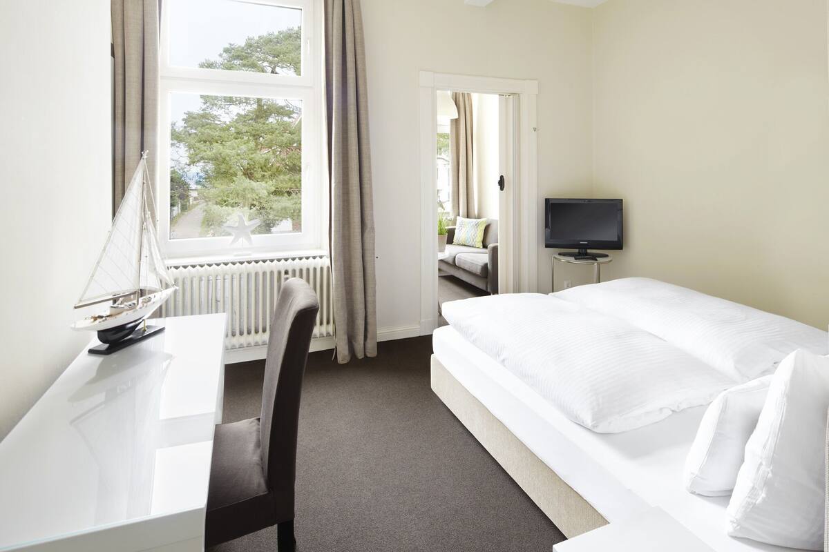 Ein Hotelzimmer mit Bett, Schreibtisch, Stuhl, Fernseher und einem Fenster mit Vorhängen.