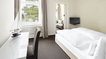 Habitación de hotel con cama, escritorio, silla, televisión y ventana con cortinas.
