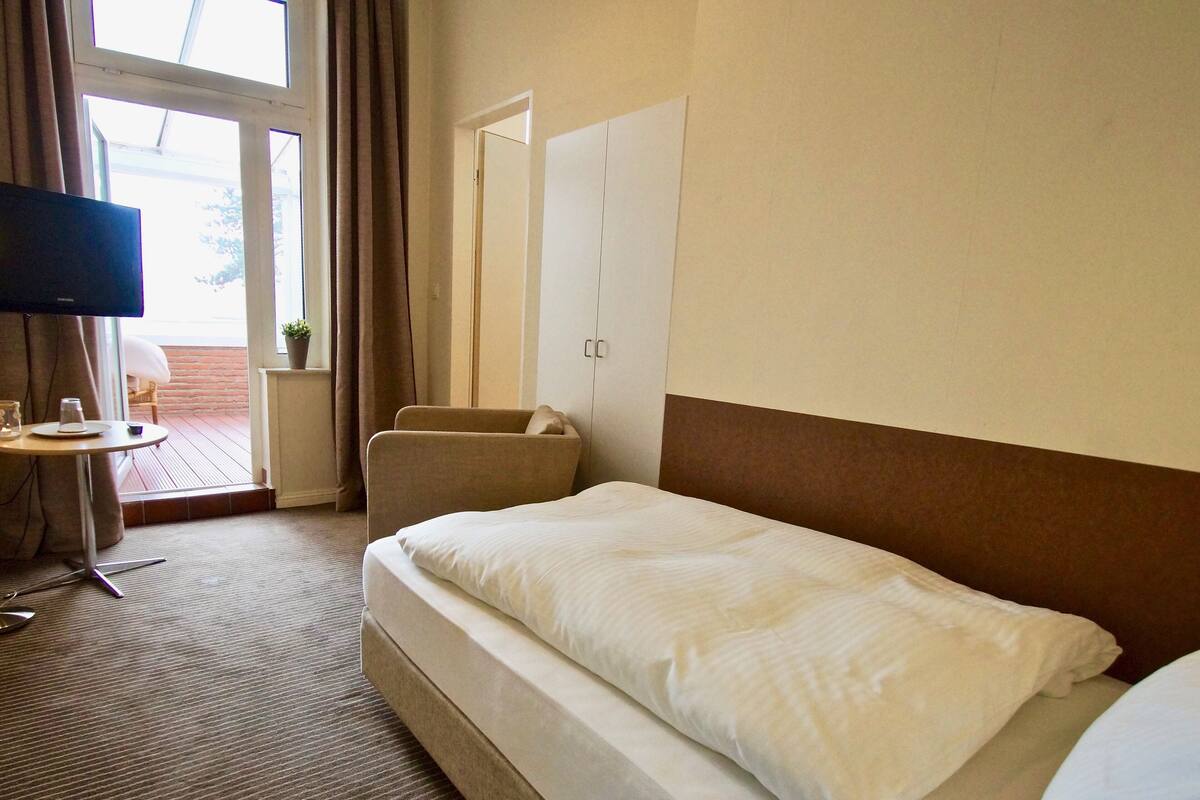 Ein Hotelzimmer mit Bett, Fernseher, kleinem Tisch mit Tasse und Untertasse sowie einem Fenster mit Vorhängen.