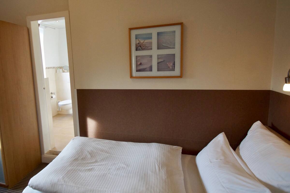 Ein Hotelzimmer mit Bett, einem gerahmten Bild an der Wand und einem durchgegangenen Tür erkennbaren Badezimmer.