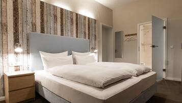 Une chambre à coucher comprenant un lit, des tables de chevet, une commode, un panneau mural en bois, une porte et un luminaire.