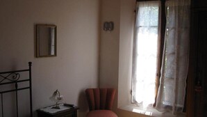 A room with a bed, a chair, a small table with a lamp, a mirror, and a window with sheer curtains. - Prisca (Ravenna)