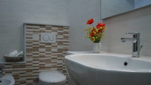 A bathroom with a toilet, bidet, and sink. There is a wall-mounted heater and a vase with flowers on the sink. - Prisca (Ravenna)