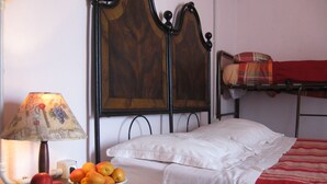 A single bed with a white sheet and a red blanket, a bedside table with a lamp and a bowl of fruit, and a wall-mounted painting. - Prisca (Ravenna)
