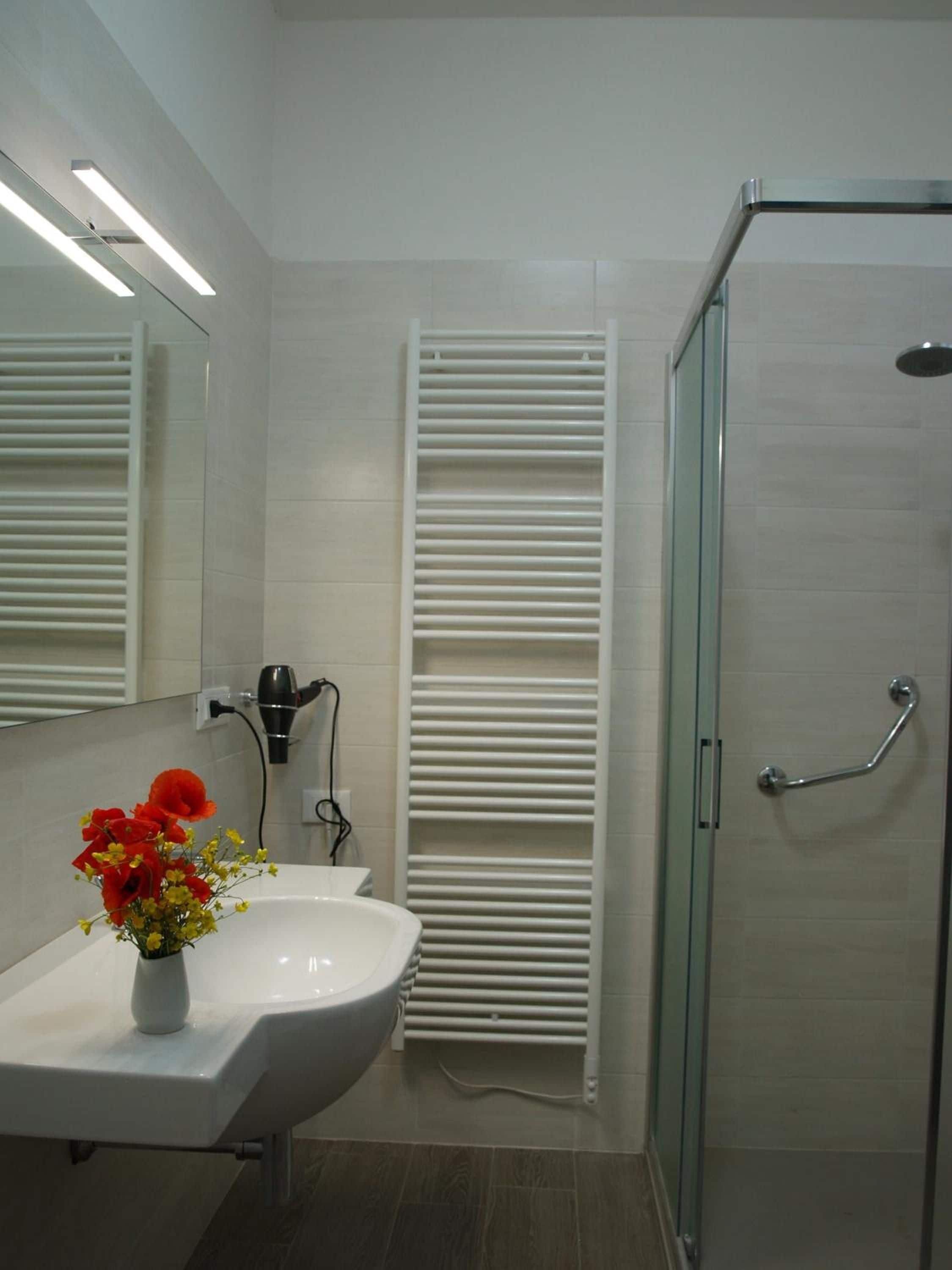 A modern bathroom with a glass shower enclosure, a white sink, and a towel rack.