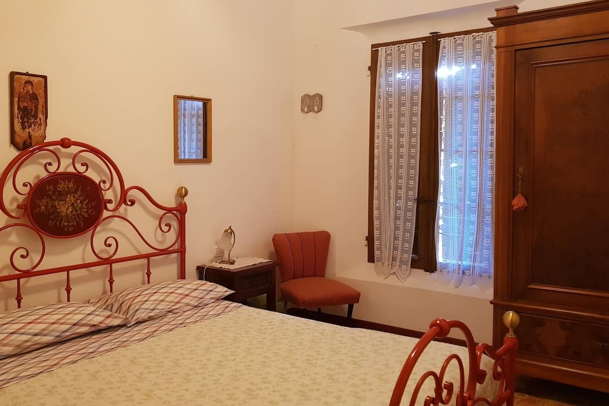 A bedroom with a bed, a nightstand, a chair, a wardrobe, and a window with curtains.