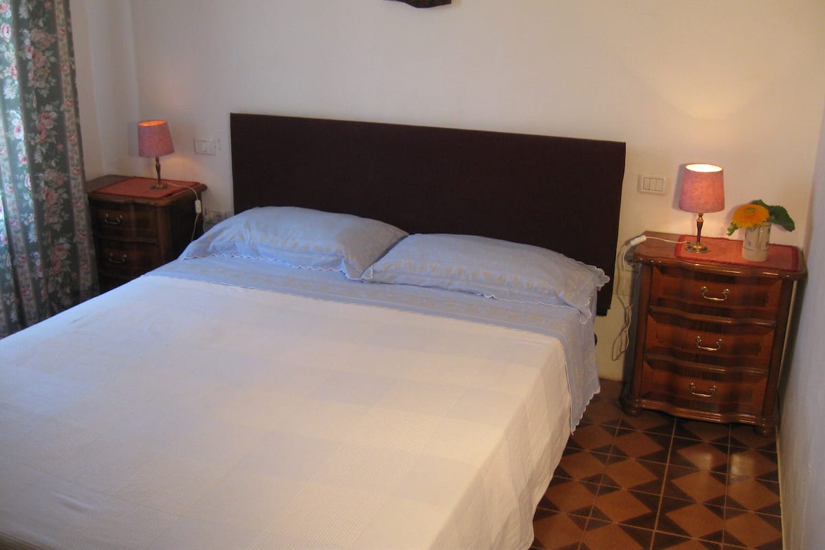 A neatly made bed with a dark headboard, two bedside tables with lamps, and a floral curtain.