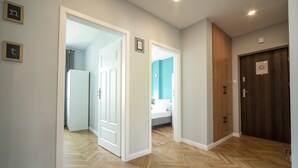 A hallway with wooden flooring, white walls, and a door leading to a bedroom with a bed and a nightstand.
