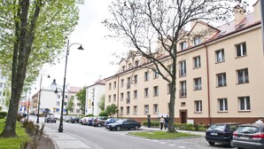 Eine Straße mit parkenden Autos und einer Reihe sandfarbener Wohngebäude.