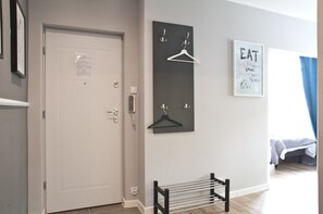 A room with a white door, a coat rack with hangers, a framed motivational poster, and a bed with a blue curtain.