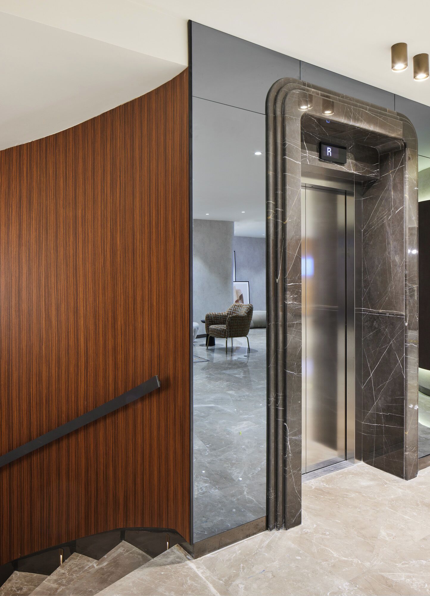 A modern elevator with a marble finish and a wooden panel wall adjacent to it.