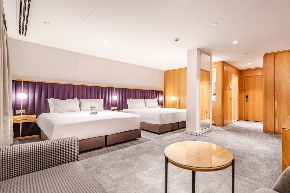 A modern hotel room with two beds, a sofa, a small table, and a TV.