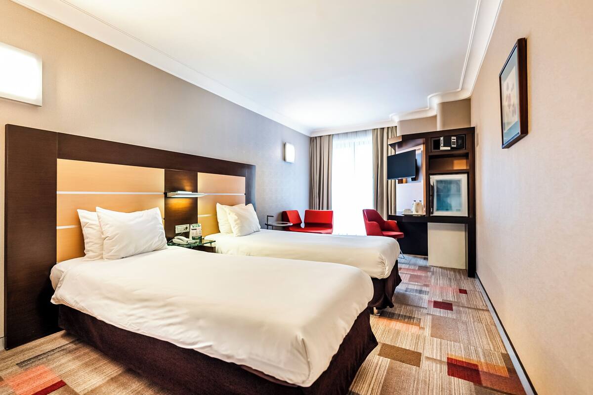 A hotel room with two beds, a desk, a chair, and a TV.