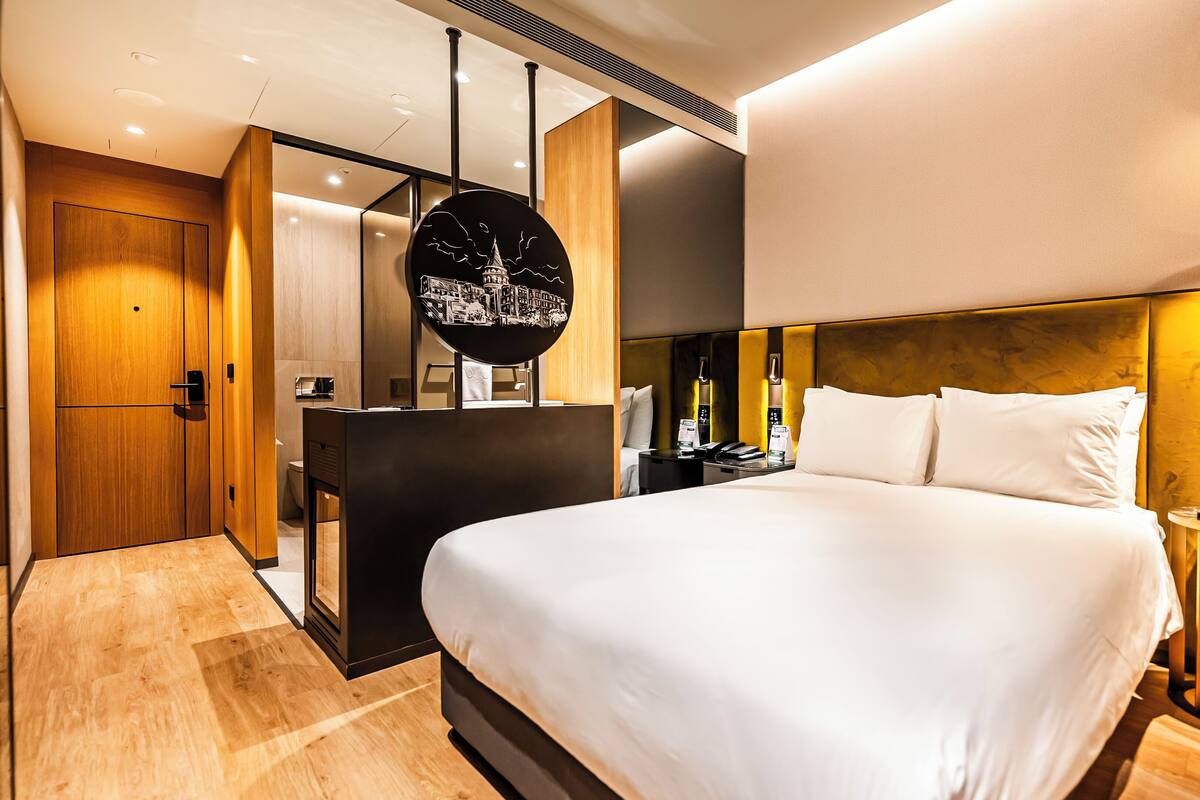 A modern hotel room with a large bed, a desk, and a mirror.