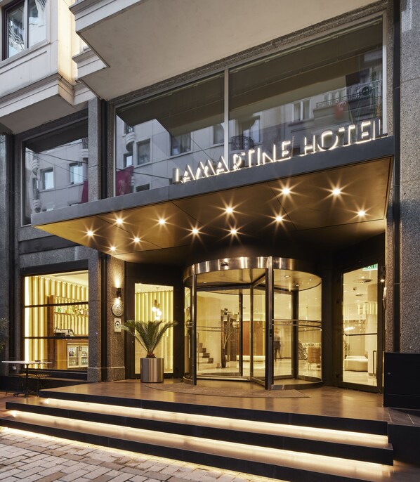A hotel entrance with a glass facade, a sign reading "LAMARTINE HOTEL," and a modern design with a curved roof and illuminated star-like lights.