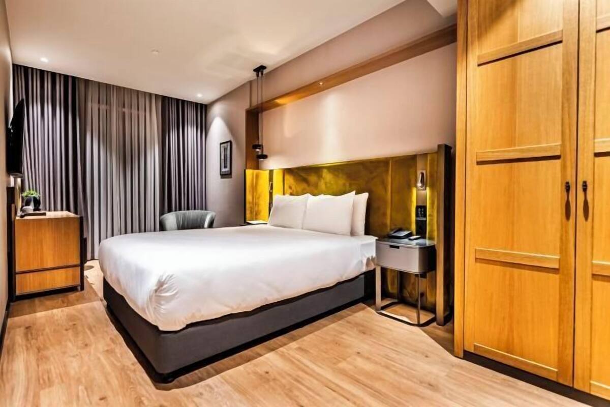 A modern hotel room with a large bed, a desk, a wardrobe, and a curtain-covered window.